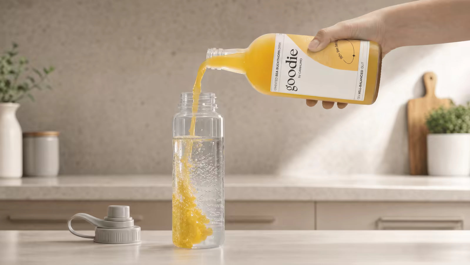Hand pouring Goodie Sea Buckthorn drink into a water bottle on a kitchen counter